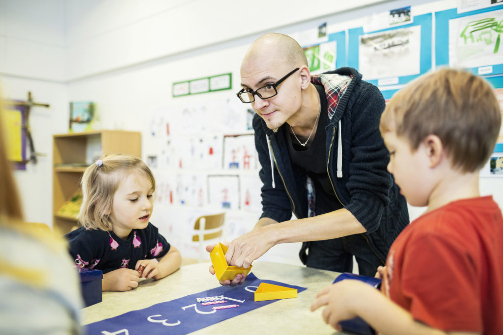 Mannlig lærer hjelper to barneskoleelever med oppgaver om tall