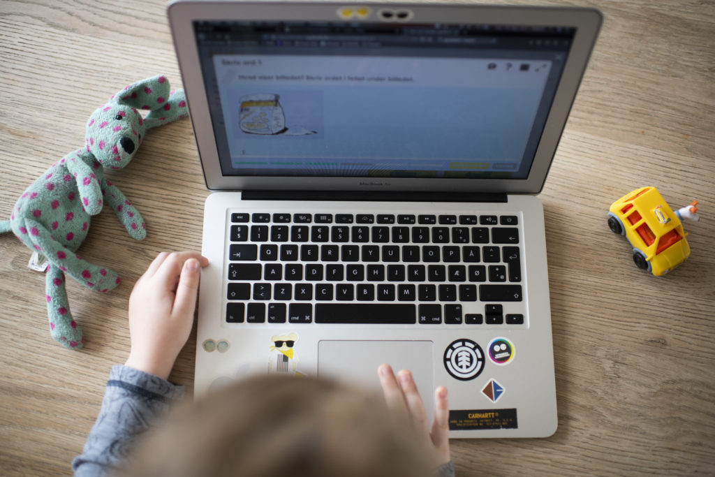 Et lite barn gjør oppgaver på PC. En bamse og lekebil på hver sin side av skjermen.