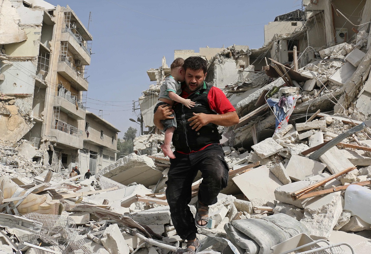 En mann bærer et barn ut av ruiner etter et bombeangrep.